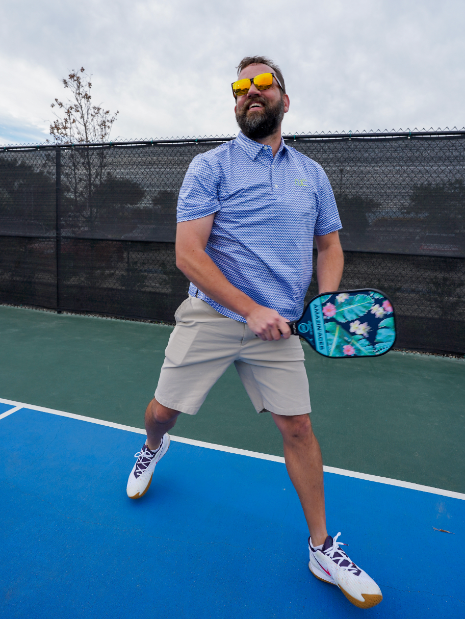 Man wearing Men's Signature Pickleball Paddle Pattern Polo in Blue playing pickleball