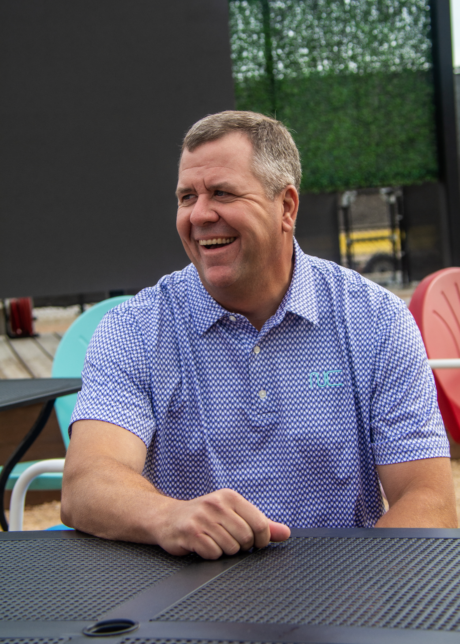 Man wearing Men's Signature Pickleball Paddle Pattern Polo in Lavender sitting at a table